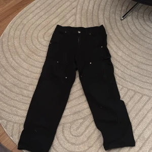 Svarta cargobyxor från Chrome Hearts - Säljer ett par svarta cargobyxor från Chrome Hearts med flera fickor och silverfärgade detaljer. Byxorna har loose passform  och klassisk cargostil, perfekt för dig som gillar streetwear och vill sticka ut med exklusiva detaljer.