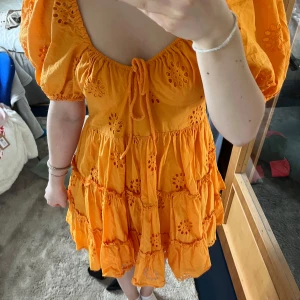 Orange kortklänning med puffärmar från Zara - Superfin orange klänning från Zara med broderade blommor och volanger. Klänningen har kort längd, puffiga kortärmar och knytning framtill.