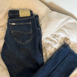  Lee jeans 30/30 - Säljer ett par klassiska mörkblå jeans från Lee med normal passform. Jeansen har fem fickor, dragkedja och knapp i midjan samt tydliga kontrastsömmar. Perfekta för dig som gillar tidlös denimstil.