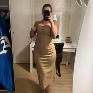 Beige axelbandslös långklänning från Zara - Säljer en beige axelbandslös långklänning från Zara. Den sitter figurnära och har en slits bak som ger både stil och rörelsefrihet. Enkel, elegant och superfin på!  Aldrig använd – prislappen sitter fortfarande kvar. Pris kan diskuteras 💕 Skriv om du vill se fler bilder!