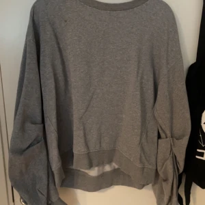 Grå sweatshirt med knytärmar från H&M - Säljer en grå sweatshirt från H&M i storlek M. Tröjan har långa ärmar med snygga knytdetaljer och en avslappnad passform. Perfekt för en chill och stilren look.