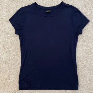Mörkblå tight t-shirt från Gina Tricot - En basic mörkblå tight t-shirt från Gina Tricot med rund halsringning och korta ärmar. Perfekt att matcha med jeans eller kjol för en enkel och stilren look. Tröjan är använd ett fåtal gånger och är i ett bra skick.