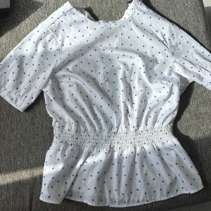 Vit blus med blå prickar från Bubbleroom - Skit Söt vit blus från Bubbleroom med blå prickigt mönster. Blusen har korta ärmar och smockad midja som ger en fin form. Den sitter jätte fint och materialet är jätte bra🩵