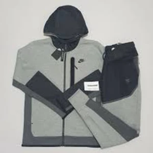 Grå Nike tech woven sällsynt  - Snygg grå hoodie jacka från Nike med svarta detaljer och dragkedja framtill. Jackan har huva och en bröstficka med dragkedja. Perfekt för en sportig stil och passar till många tillfällen. Plus byxan som är woven då det är två olika material båda är strl s 100% äkta finns kvitto 