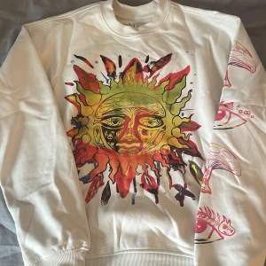 Vit Sublime sweatshirt med soltryck - Kräm vit lån ärmad tröja med stort tryck på framsidan, baksida och även på armarna perfekt till dig som gillar färger och stora tryck. Och den passar även bra  till en lite kyligare sommarkväll. Den är i storlek Xs men passar perfekt som en S
