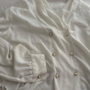Elegant blus/skjorta - Säljer en v-ringad jätte fin vit blus/skjorta med eleganta guld &vita knappar. Inga defekter.  Jag säljer den då jag köpte den till min mamma som inte ville ha den så den är aldrig använd och materialet är jätte skönt och bra✨✨bild på skickas privat vid intresse för min mamma måste ha på den eftersom den är för stor för mig. Pris kan diskuteras💛