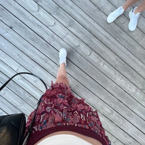 Röd mönstrad volangkjol - Säljer en kort röd kjol med färgstarkt mönster och volangdetaljer.Den är  barnstorlek men Kjolen har resår i midjan som gör att den är stretchig och passar nästan alla kroppsformer, den är även lång i längden, jag är 1,63 ungefär men passar ändå och till och med brukar vika ner kanten för att inte få den så lång, så med detta den passar nästan alla. Kjolen är köpt för ungefär 2 år sedan på Lindex och andvänd mycket men inget tecken på andvändning . Kom privat för fler bilder och frågor om storle