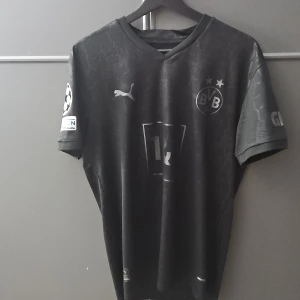 Borussia Dortmund svart matchtröja Reus 11 - Säljer en svart Borussia Dortmund fotbollströja med Reus 11 på ryggen. Tröjan har korta ärmar, BVB-logga, Puma-logga och Champions League-märke på ärmen. Snygga detaljer och tryck i vitt och grått. Priset går att prata om:)