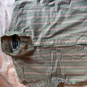 Grön- och vitrandig skjorta från Ralph Lauren - Säljer en grön skjorta från Ralph Lauren med vita och rosa ränder. Klassisk krage, knäppning framtill och broderad logga på bröstet. Skjortan har lång ärm och är i bomull. Perfekt för dig som gillar stilrena plagg med lite färg.