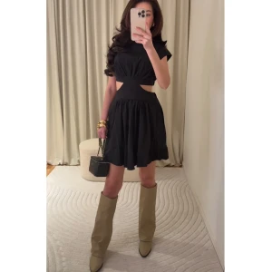 Svart kortklänning med cut-out detaljer - Trendig svart kortklänning med cut-out detaljer i midjan och rund halsringning. Klänningen har korta ärmar och en lätt utställd kjol. Perfekt för dig som vill ha en modern och stilren look. passar xs-m då den är flowy och inte tight.