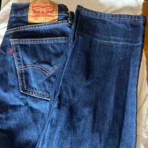 Blåa levi’s jeans 505 - Klassiska blå Levi's 505 jeans med raka ben och normal passform. Jeansen har fem fickor, dragkedja och knapp i midjan samt tydliga kontrastsömmar. Perfekta för en avslappnad stil och tillverkade i slitstarkt denimtyg. W30,L32