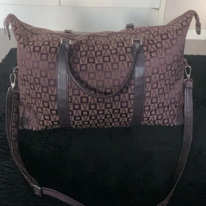Brun weekendbag från Vezzano - Stor brun weekendbag från Vezzano med geometriskt mönster i svart. Väskan har både handtag och justerbar axelrem samt dragkedja upptill. Bra skick med rymligt huvudfack och innerficka med dragkedja.