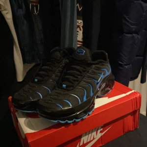 Nike Air Max Plus TN med blå detaljer - Säljer ett par Nike Air Max Plus TN sneakers i svart med blå detaljer och TN-logga på hälen. Skorna har en vågig design, synlig Air Max-dämpning och platt sula. Perfekta för dig som gillar sportig och modern stil.