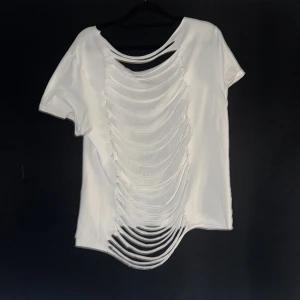 Vit t-shirt med slitsad rygg - Säljer en vit t-shirt med korta ärmar och unik slitsad design på ryggen. T-shirten har rund halsringning och är tillverkad i mjukt bomullsmaterial. Perfekt för dig som vill sticka ut med en edgy och trendig look. Vill man ha den oversize passar den mer åt S men tajt så är de mer en L🌸