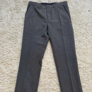 Grå kostymbyxor  - Snygga grå kostymbyxor med klassisk rak passform och pressveck. Byxorna har hällor för bälte, knäppning med knapp och dragkedja samt sidofickor. Jätte snygga och stiliga 