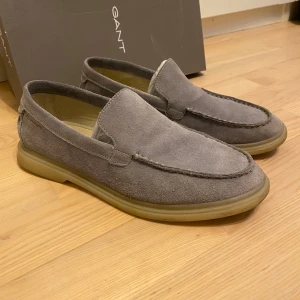 mockaloafers från Gant - Säljer ett par stilrena loafers från Gant i mjuk mocka och färgen dove blue. Skorna har en klassisk design med rund tå och platt sula, perfekt för en avslappnad men snygg look. Passar bra till både jeans och chinos.