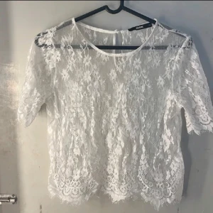 Vit spetstopp - Säljer en söt vit spetstopp från  Bik Bok i genombruten spets med blommigt mönster. Blusen har rund halsringning, korta ärmar och knapp i nacken. Perfekt för en romantisk look!