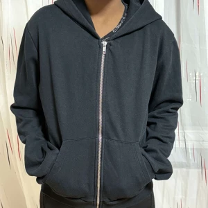 Svart hoodie med dragkedja - En enkel svart hoodie med dragkedja framtill och huva. Tröjan har långa ärmar och två fickor på sidorna. Perfekt för en avslappnad stil. Ny och inte använd