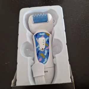 Elektrisk fotfil SODY SD 8005 - Elektrisk fotfil med blå sliprulle och färgglad design. Drivs med batteri och har två olika sliprullar för effektiv borttagning av förhårdnader. Inkluderar rengöringsborste och extra rulle. Perfekt för mjuka och lena fötter.