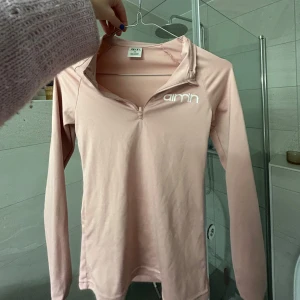 Ljusrosa långärmad träningströja från Aim'n - Säljer en ljusrosa långärmad träningströja från Aim'n med halv dragkedja framtill och logga på bröstet. Perfekt för träning eller som ett snyggt lager. Materialet är mjukt och stretchigt.