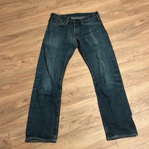 Levis 514 blå jeansbyxor - Klassiska blå Levis 514 jeans med raka ben och normal passform. Byxorna har fem fickor, knappgylf och tydliga slitningar för en vintage look. Perfekta för dig som gillar tidlös denimstil.
