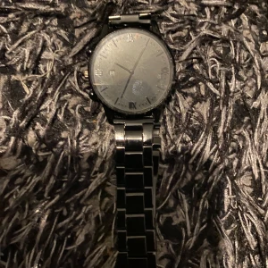 Svart armbandsur med metallänk - Stilren svart klocka med rund urtavla och romerska siffror. Klockan har en svart metallänk och datumvisning. Passar dig som gillar en klassisk och enkel design.