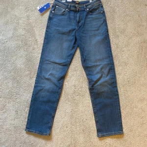 Blå jeans från Jack & Jones - Snygga blå jeans från Jack & Jones med klassisk femficksdesign och raka ben. Jeansen har orangea kontrastsömmar, knappgylf och normal passform. Perfekta för en avslappnad stil.