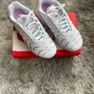 Nike Air Max sneakers i vitt och rosa - Säljer ett par fräscha Nike Air Max sneakers i vitt med rosa detaljer och grå sula. Skorna har klassisk snörning och en sportig design med synlig Air-dämpning. Perfekta för dig som gillar stilrena och bekväma sneakers.