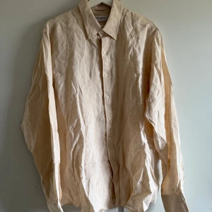 Beige linneskjorta från John Henric - Säljer en stilren beige skjorta i linne från John Henric. Skjortan har klassisk krage, knäppning framtill och långa ärmar. Perfekt för en avslappnad men ändå uppklädd look. Storlek 44 mycket bra skick. Nypris 999kr