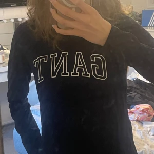 Mörkblå långärmad tröja från GANT - Säljer en mörkblå långärmad tröja från GANT med vit logotyp framtill. Tröjan har en klassisk rund halsringning och är tillverkad i mjuk bomull. Tröjan är aldrig använd och har inga defekter💕