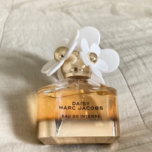 Daisy Eau So Intense parfym från Marc Jacobs - Säljer en Daisy Eau So Intense parfym från Marc Jacobs. Flaskan är guldig med en transparent nedre del och har ett unikt lock dekorerat med vita och guldiga blommor. Doften är fräsch och blommig, perfekt för dig som gillar eleganta parfymer.