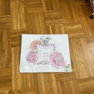 Poster med parfymflaska och blommor - Snygg poster med motiv av en parfymflaska omgiven av rosa och lila blommor. Perfekt som väggdekoration för att ge rummet en feminin och trendig touch. Tryckt på vitt papper med mjuka pastellfärger och stilren design.