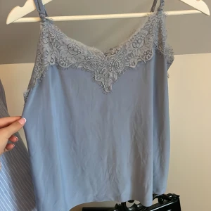 Ljusblå topp med spets🌟 - Säljer en ljusblå linnetopp från Amisu med vacker spetsdetalj längs urringningen. Toppen har justerbara axelband och är perfekt för varma dagar. Snygg och enkel att matcha till olika outfits!