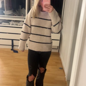 Beige stickad tröja med svarta ränder - Mysig beige stickad tröja med svarta horisontella ränder. Tröjan har lång ärm och bred ribbad mudd vid ärmslut och nederkant. Perfekt för kyligare dagar och enkel att matcha med jeans eller kjol.