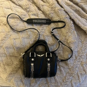 Svart handväska från Zadig & Voltaire -  svart handväska från Zadig & Voltaire med silverdetaljer, dragkedjor och nitar. Axelrem med broderad logga och små handtag. Får med påse som den ligger i 