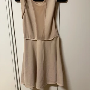 Beige ärmlös klänning med markerade sömmar - Säljer en beige ärmlös klänning med markerade sömmar och lätt utsvängd kjol. Klänningen har en enkel design och är tillverkad i ett mjukt, stretchigt material. Perfekt för varma dagar eller som basplagg i garderoben.