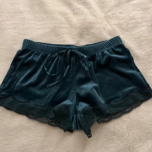 Mörkgröna sammets-shorts med spets - Mysiga mörkgröna shorts i sammetsmaterial med spetsdetaljer längs bensluten och snörning i midjan. Perfekta för en avslappnad och stilren look.