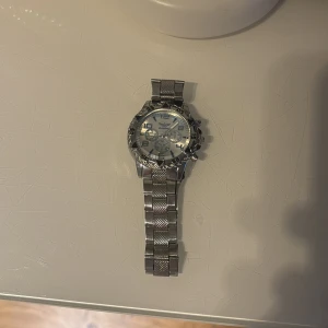 Silverfärgad herrklocka med metallarmband - Stilren herrklocka i silver med robust metallarmband och detaljerad urtavla. Klockan har flera knappar på sidan och en sportig design som passar till många tillfällen.