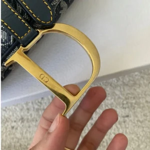 Dior Saddle Bag i blått mönster - Säljer en ikonisk Dior Saddle Bag med blått och vitt monogrammönster. Väskan har guldfärgade metalldetaljer, bland annat det klassiska D-spännet, och mörkblåa läderdetaljer med gul söm. Perfekt statement piece för dig som vill sticka ut.