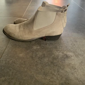 Beige mocka chelsea boots - Säljer ett par stilrena beige chelsea boots i mocka med elastiska paneler på sidorna och låg klack. Skorna har rund tå och klassisk siluett, perfekta för att lyfta din outfit.