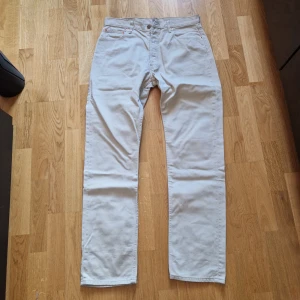 Beige Levi's 551 jeans - Säljer ett par klassiska beige Levi's 551 jeans med rak passform. Byxorna har fem fickor, bälteshällor och stängs med dragkedja och knapp. Perfekta för dig som gillar en tidlös och avslappnad stil.