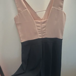 Beige och svart långklänning med v-ringning - Säljer en elegant långjumpsuit  med beige överdel och svart nederdel. Klänningen har djup v-ringning både fram och bak samt markerad midja. Perfekt för bal eller festliga tillfällen. Lite puder rosa mer än beige 