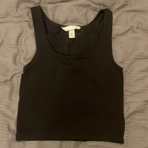 Svart croppad linne från H&M - Ett enkelt och svart croppat linne från H&M. Toppen har breda axelband och rundad halsringning. Väldigt basic och bra!