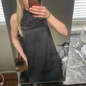Svart ärmlös satinblus med rosett i nacken - Snygg svart blus i glansigt satinmaterial med hög hals och ärmlös design. Använt fåtal gånger och är i jätte bra skick. Perfekt för att lyfta vilken outfit som helst.💞💞