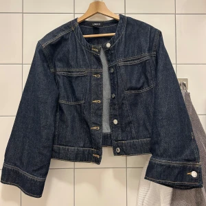 Mörkblå jeansjacka  - Säljer en mörkblå croppad jeansjacka från Lindex med vida ärmar och rund halsringning. Använd endast två gånger.