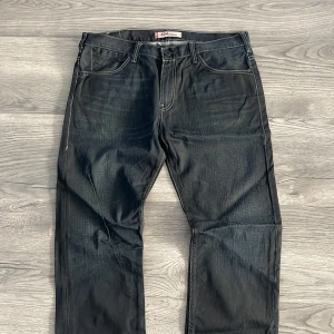 Svarta jeansbyxor från Levi's 501 - Klassiska svarta jeansbyxor från Levi's 501 med raka ben och femficksmodell. Byxorna har normal passform och synliga kontrastsömmar. Perfekta för en stilren och tidlös look.