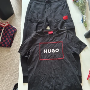 Svart Hugo boss dress - Svarta mjukisbyxor från Hugo med dragsko i midjan och röd logotyp-patch på benet. Byxorna har en avslappnad passform och är perfekta för en chill stil. Matcha med en hoodie eller t-shirt för en hel look.