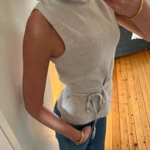 Beige ärmlös polotopp med knytband - Säljer en beige ärmlös polotopp med knytband i midjan. Bandet går även att ta bort om man vill det🙌🏼🥰.