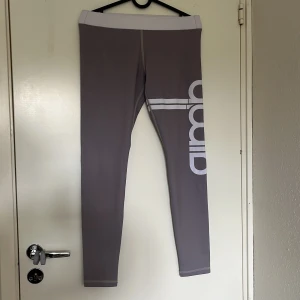 Grå träningstights från aim'n - Snygga grå tights från aim'n med bred vit midja och vit logga längs benet. använda men inga skavanker förutom lite nopprig på ett ställe