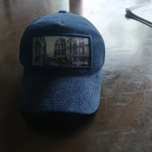 Mörkblå keps från Zantiore - Snygg mörkblå keps från Zantiore med ett stadsmotiv framtill. Kepsen har böjd skärm och mesh på insidan för extra ventilation. Perfekt accessoar för en avslappnad stil.